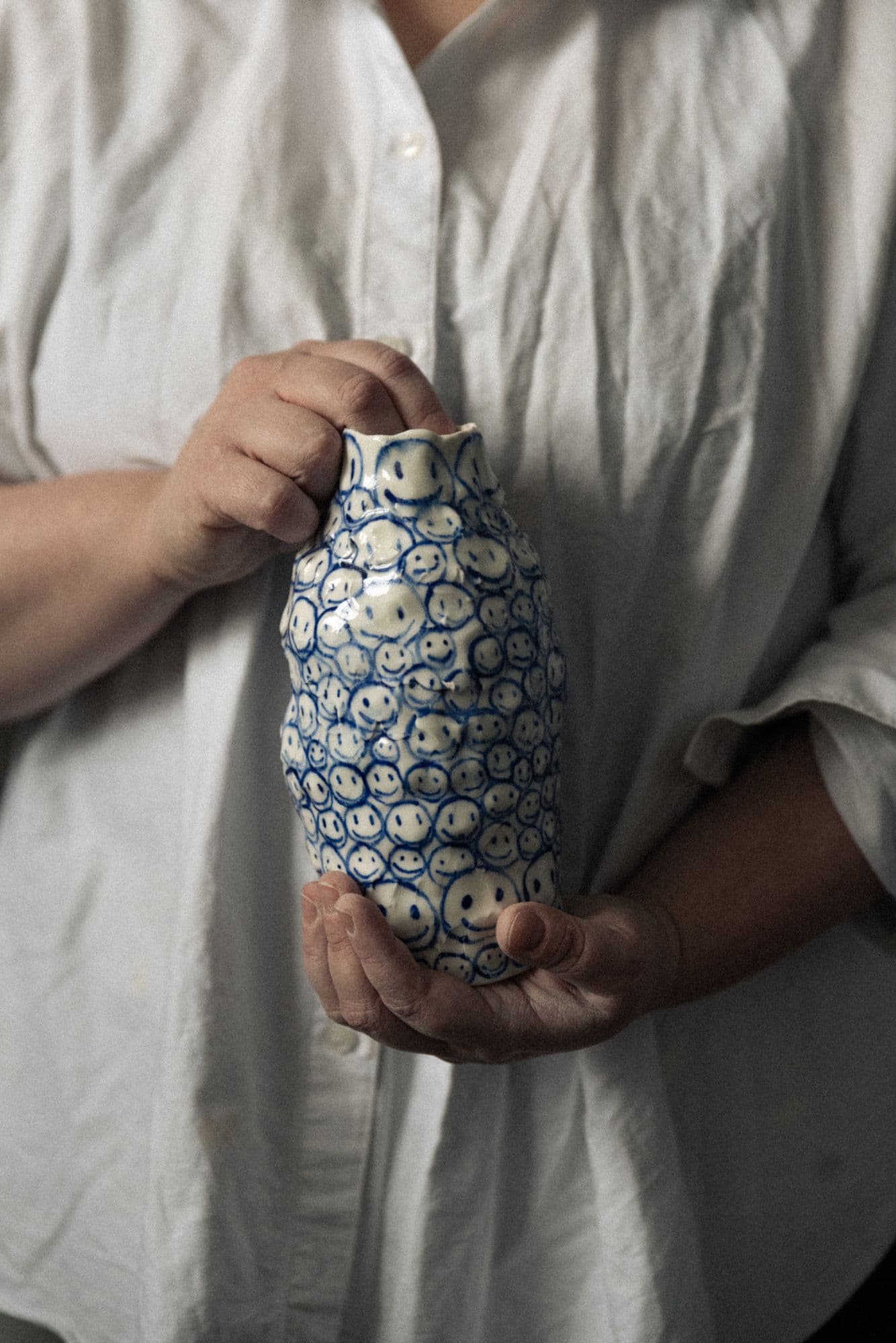 Sofi Gunnstedt holding a hand-painted ceramic vase covered in small smiley faces