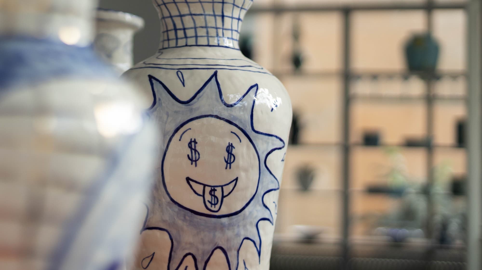 Close-up of a ceramic vase with a hand-drawn sun face with dollar-sign eyes