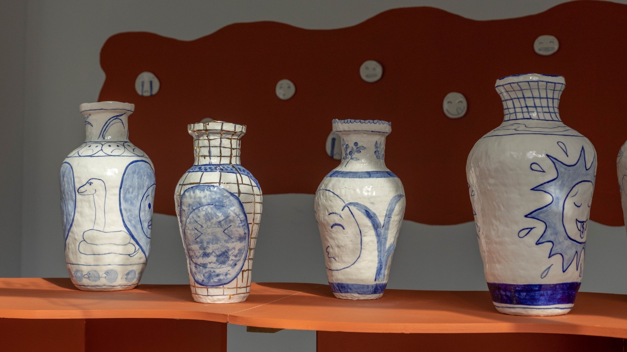 Hand-painted ceramic vases by Sofi Gunnstedt, displayed on a shelf alongside small wall-mounted ceramic faces
